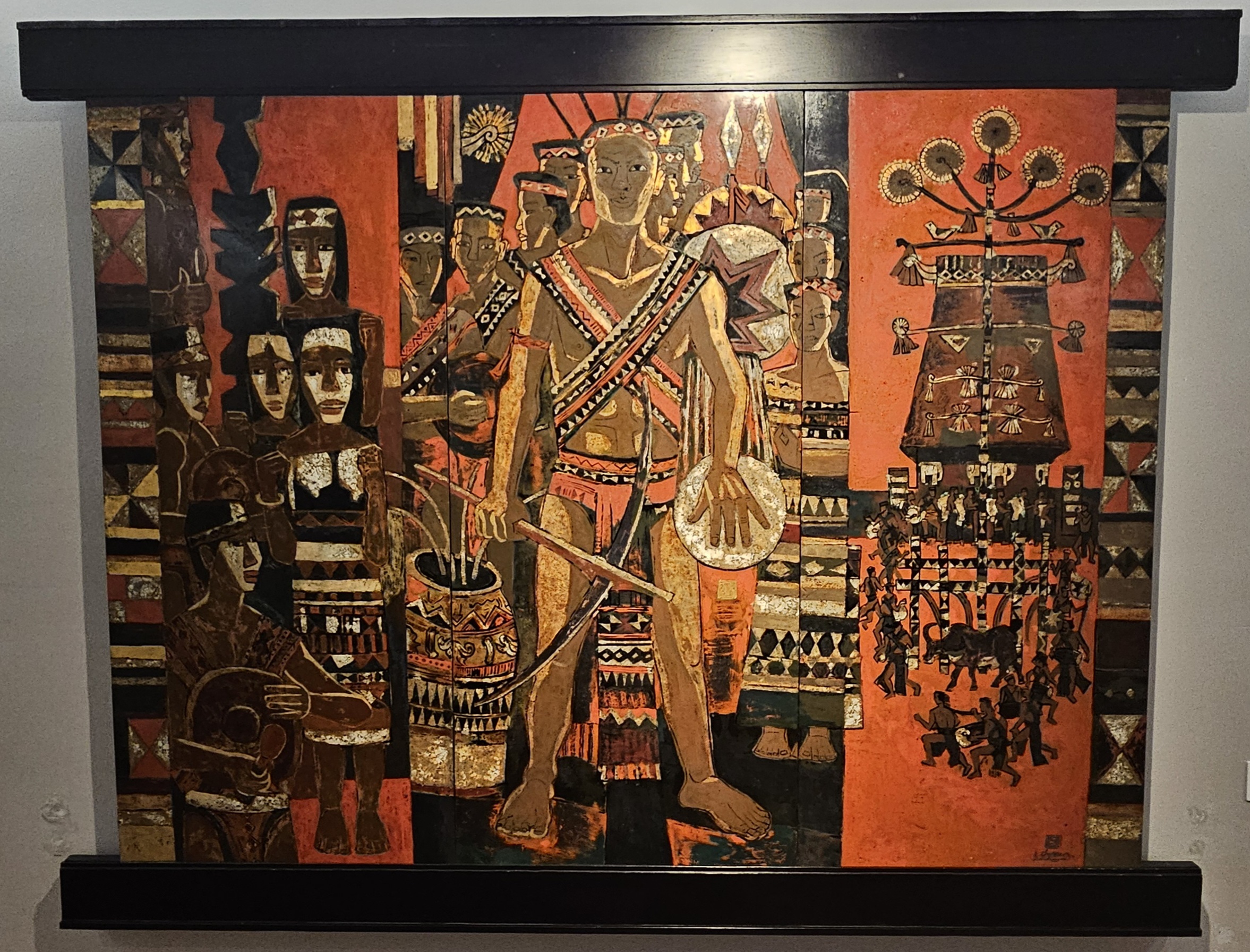 A colorful mural depicting a central figure adorned in tribal attire, surrounded by various abstract patterns and other figures, suggesting a cultural celebration or ritual.