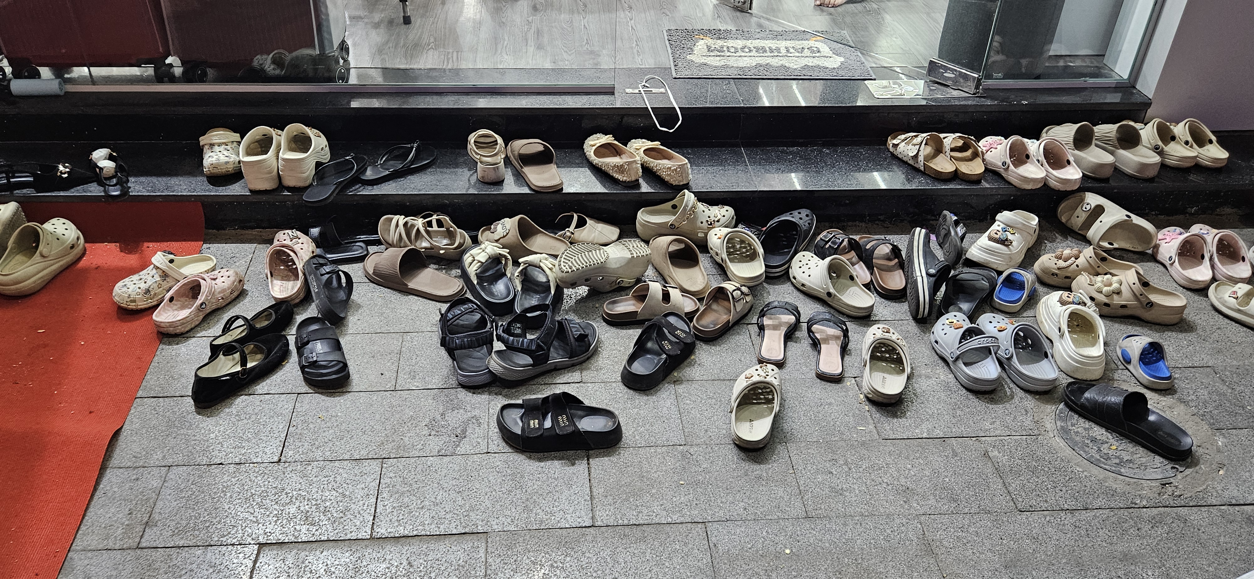 A variety of shoes scattered on the ground outside a store, including sandals, clogs, and flip-flops in different colors and styles.