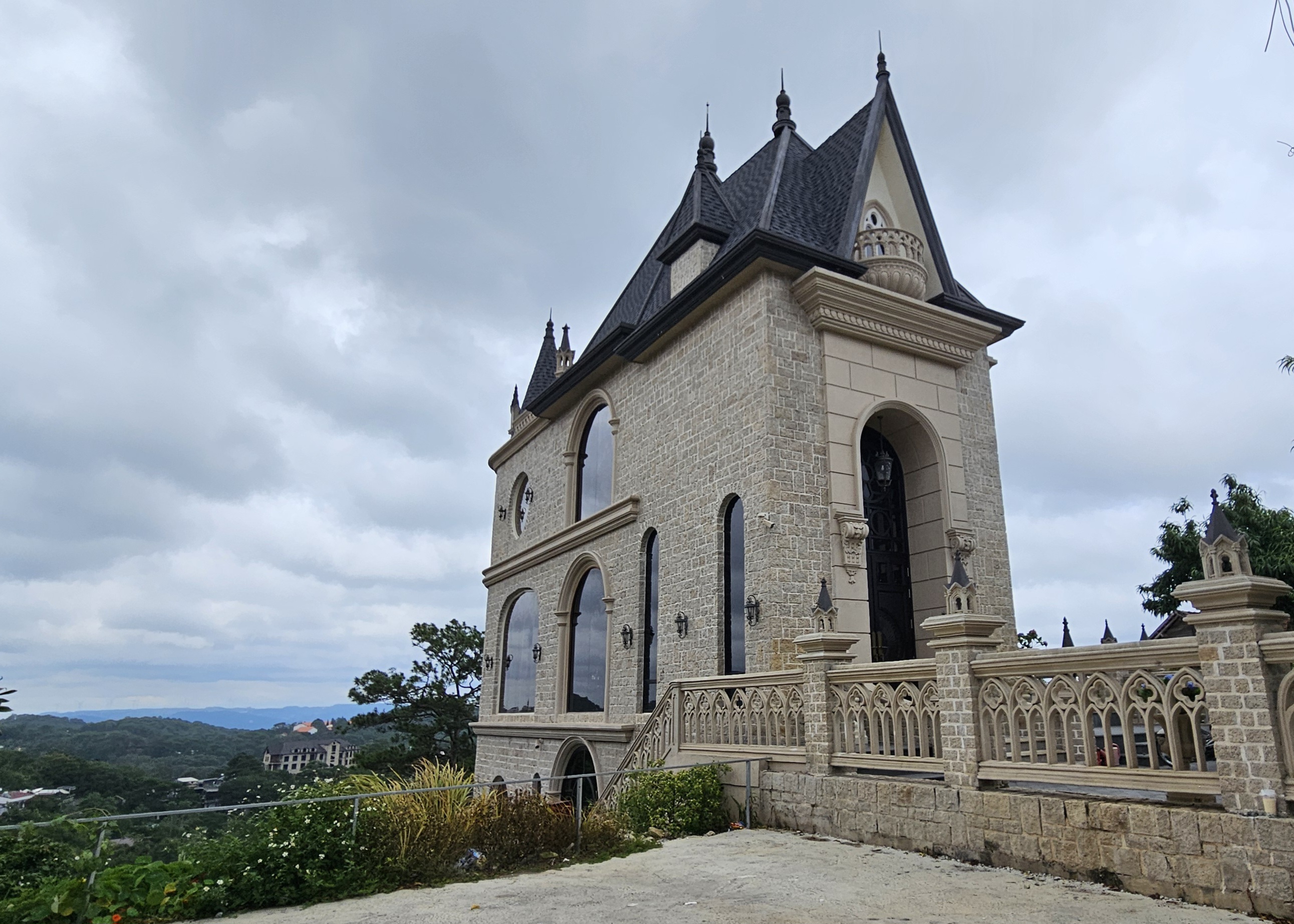 A large stone mansion with intricate architectural details, featuring pointed roofs and arched windows, set against a cloudy sky.