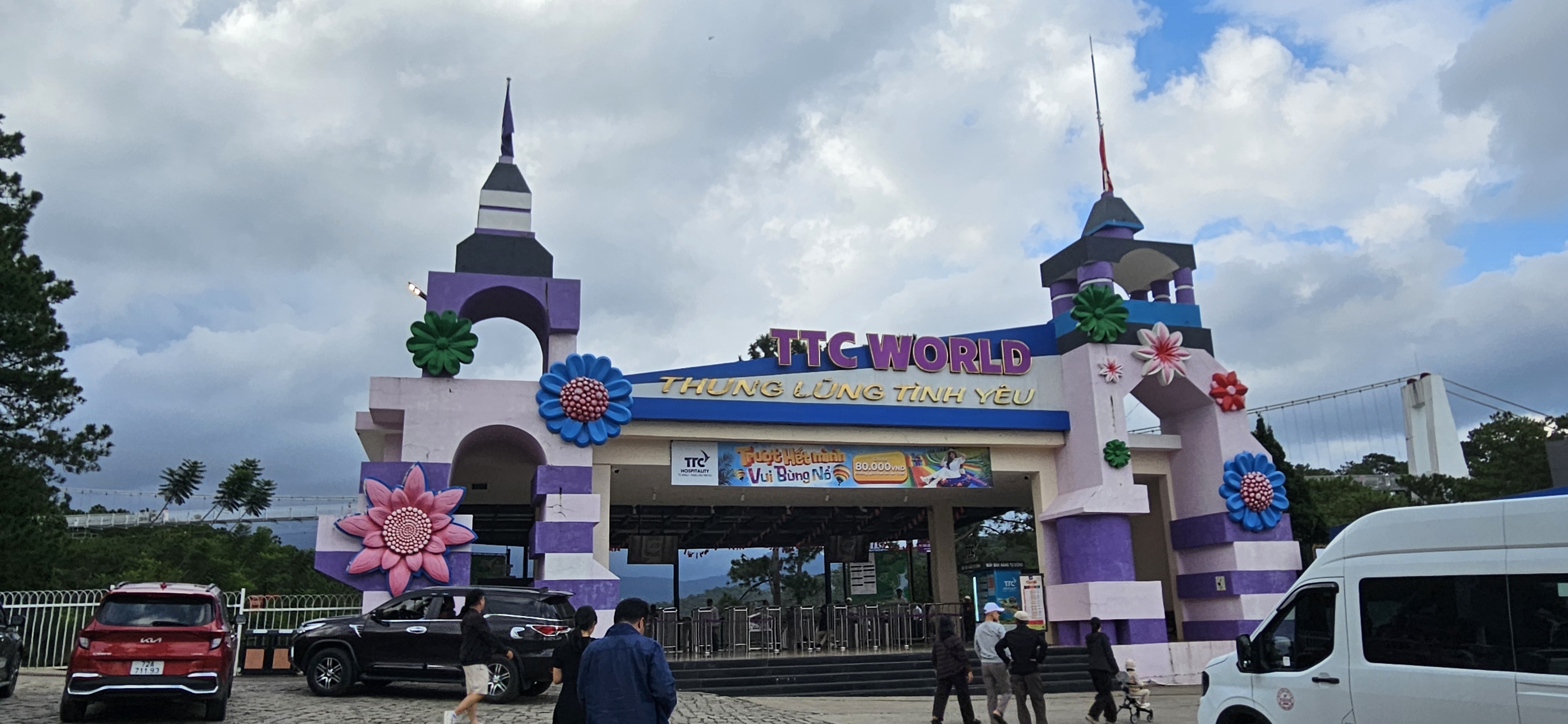 Entrance gate of TTC World, featuring colorful flowers and two towers with a blue sky backdrop.
