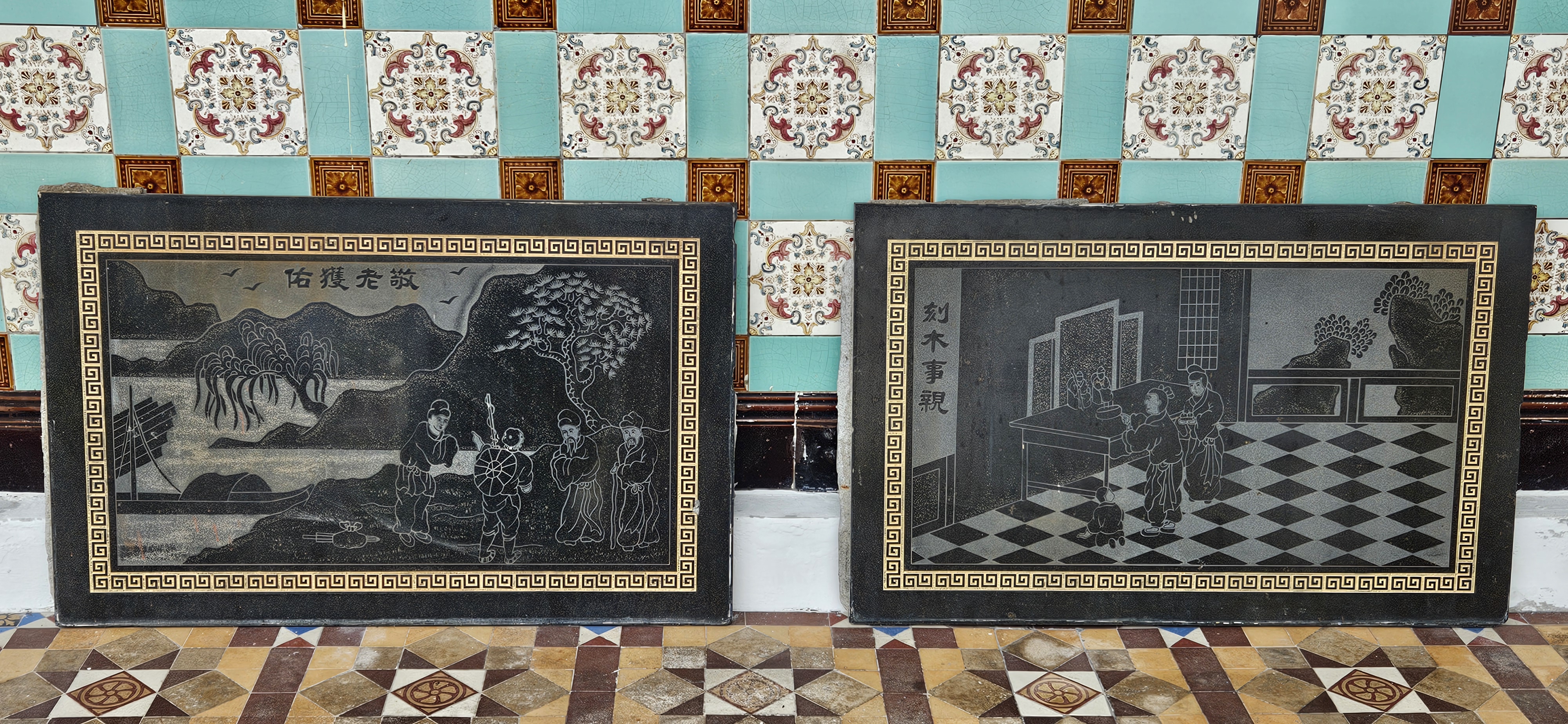 Two decorative stone plaques with engravings, one depicting figures near a mountainous landscape and a boat, the other showing figures inside a room with a checkered floor and decorative elements, set against a patterned wall.