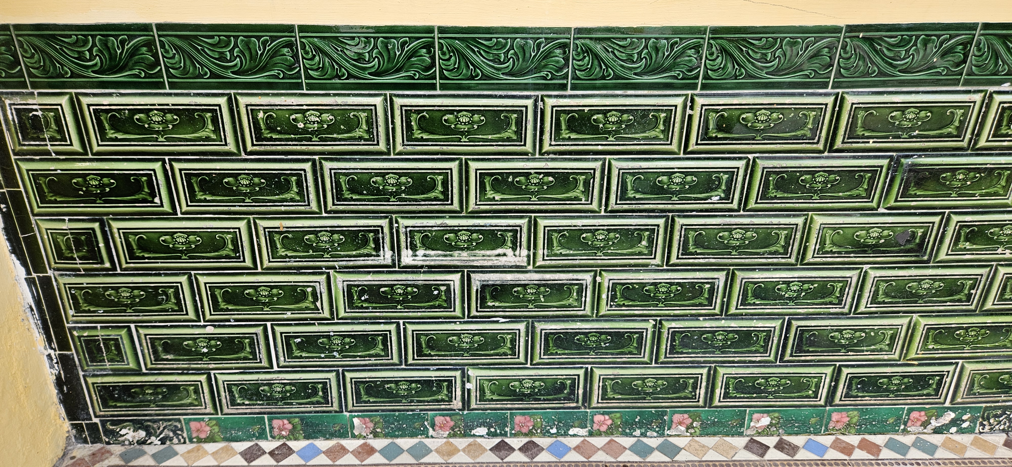 Decorative green tile wall featuring embossed floral patterns and a colorful patterned lower border.