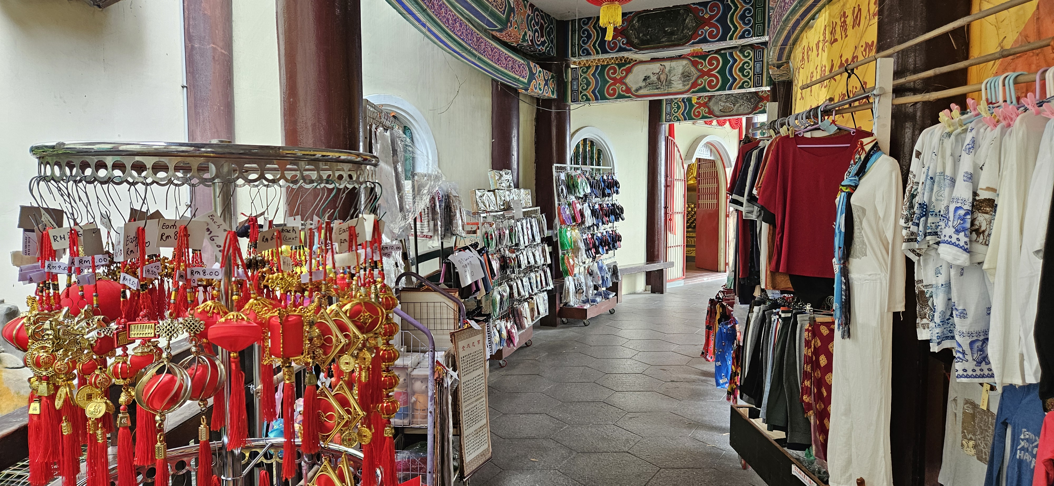 Interior view of a market aisle featuring red decorative items on display, with clothing racks displaying various apparel on both sides.