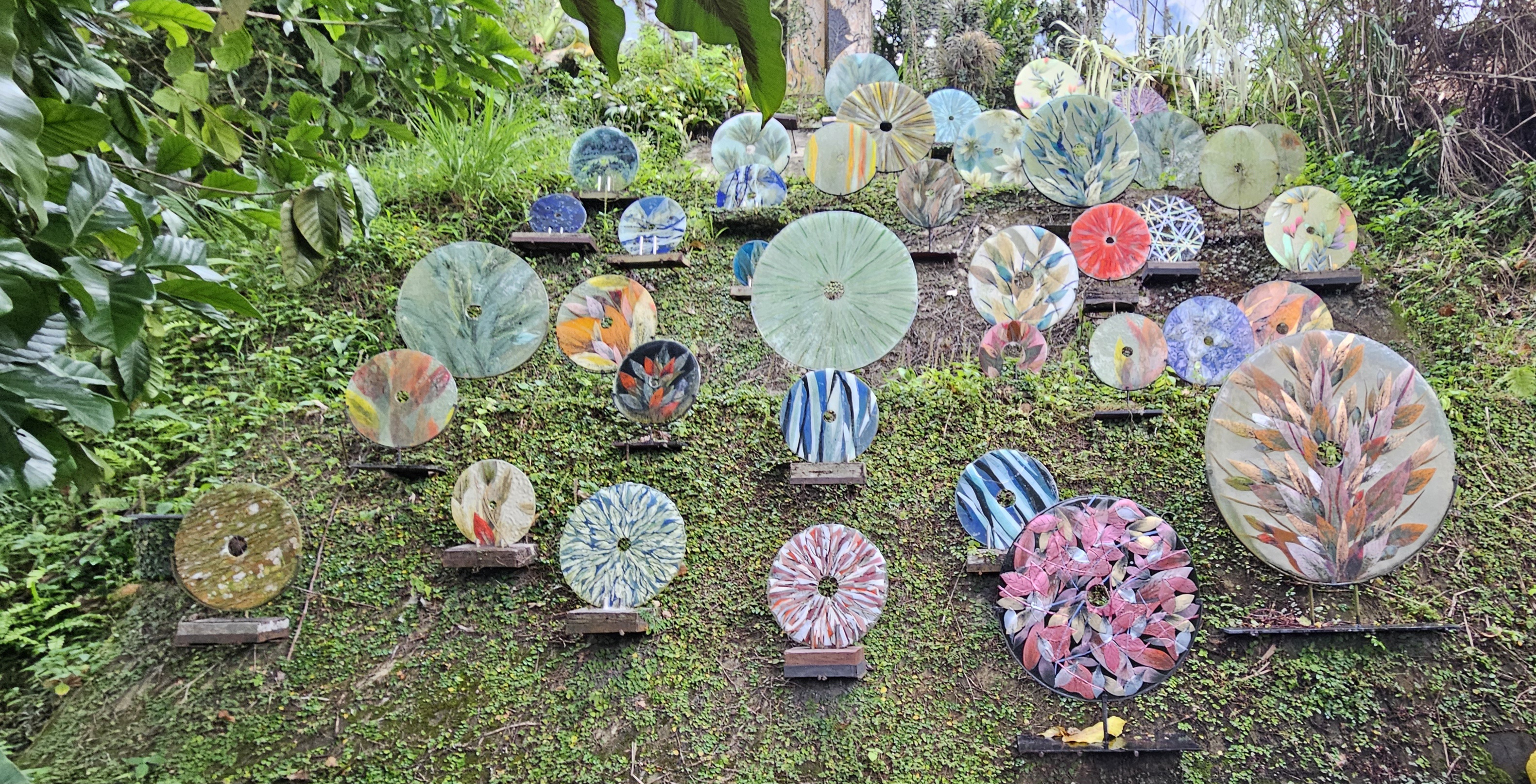 A colorful display of circular artistic plates arranged on a grassy hillside, featuring various floral and abstract designs.