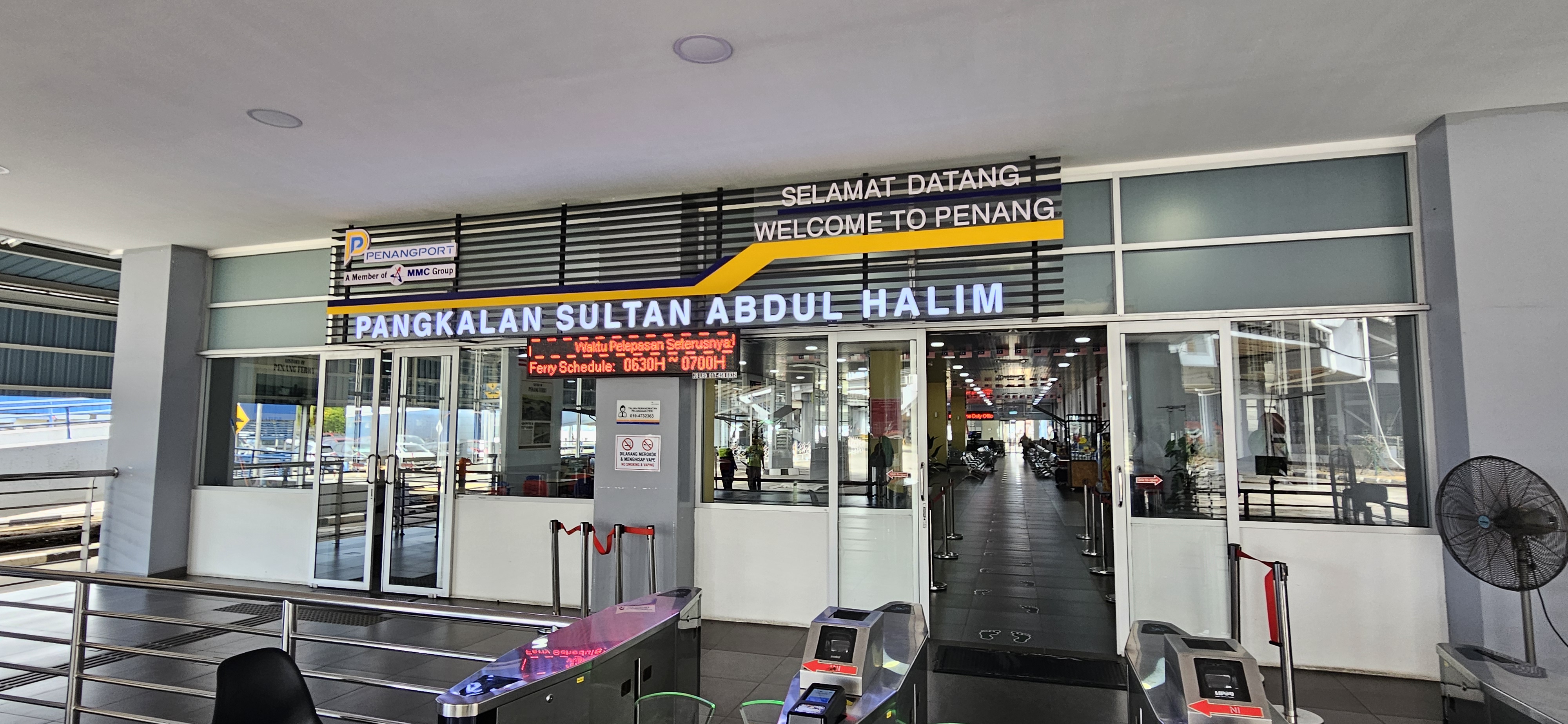 Entrance to Pangkalansultan Abdul Halim, a ferry terminal in Penang, Malaysia, featuring signage in both English and Malay. The terminal has a modern design with seating and facilities visible inside.