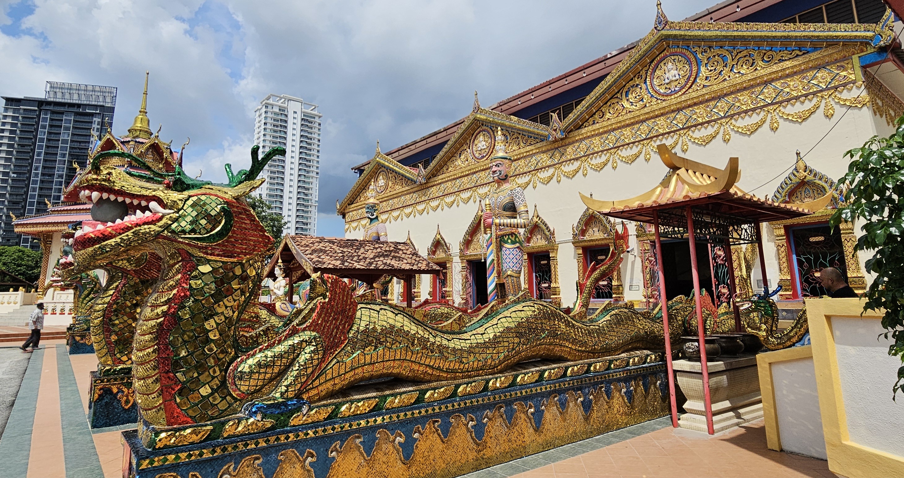 A colorful dragon sculpture in front of an ornate temple with gold accents, surrounded by modern buildings in the background.
